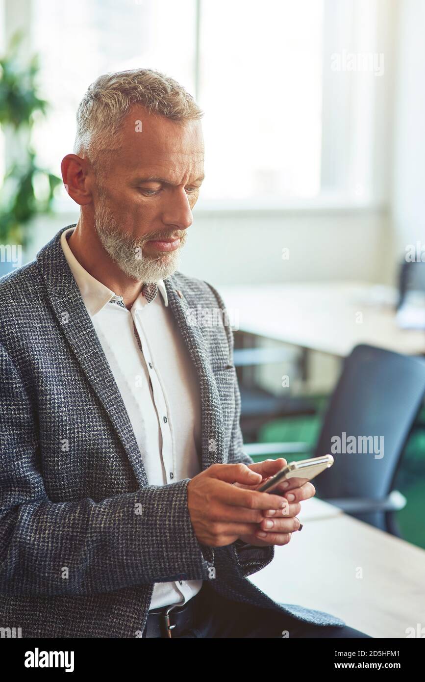 Confident mature businessman in formal wear using his smartphone while ...