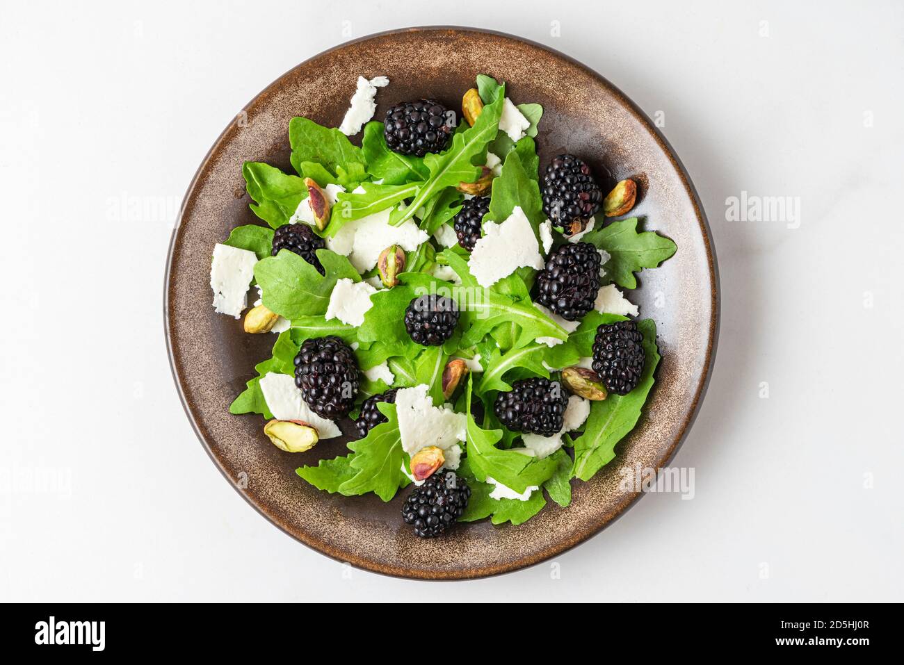 Fresh salad with arugula, goat cheese, blackberries and pistachios in a plate on white background. top view. healthy diet food Stock Photo