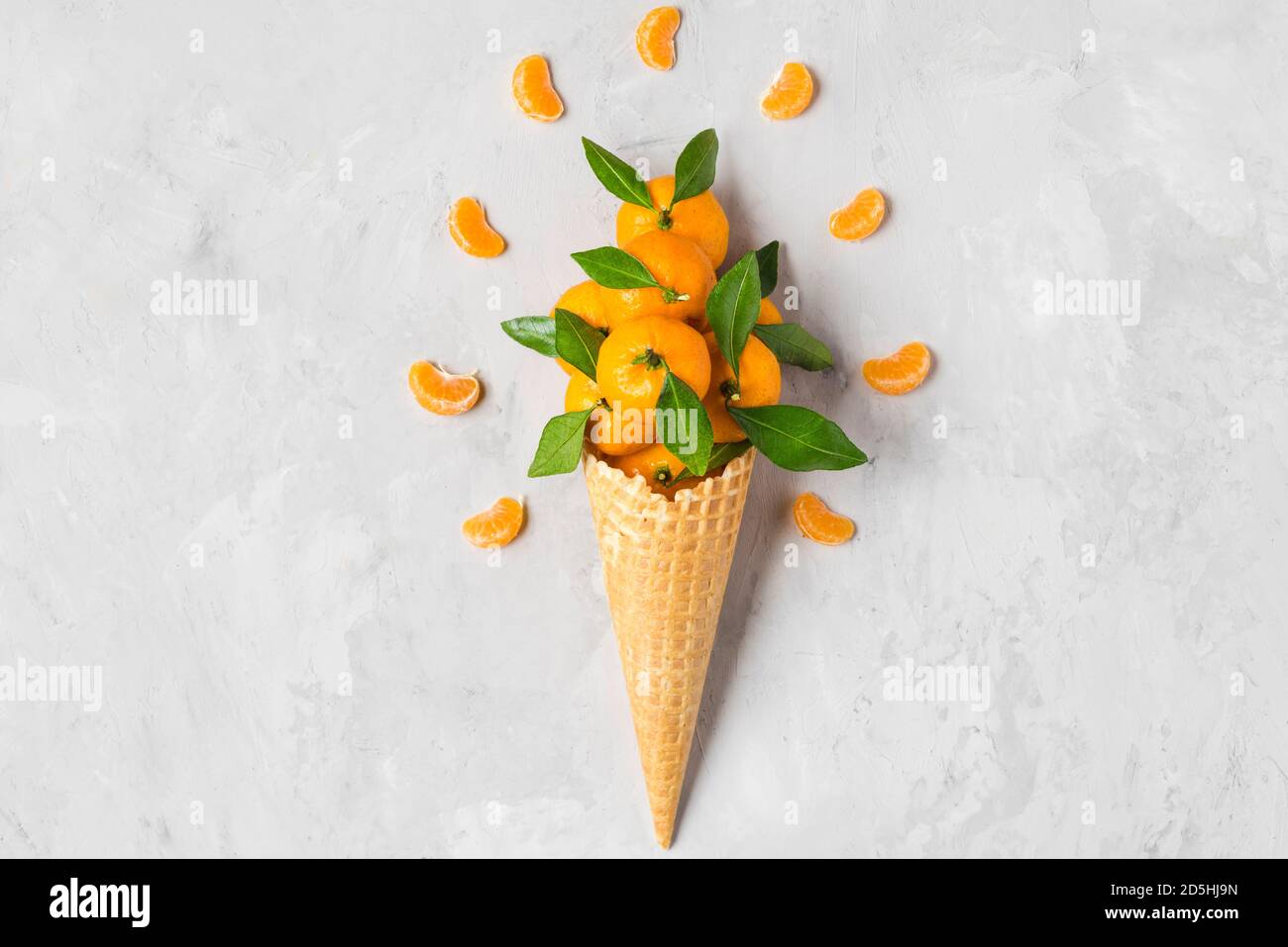 mandarin orange or tangerine fruits in waffle ice cream cone with slices on concrete background. winter Christmas food concept. top view. flat lay Stock Photo