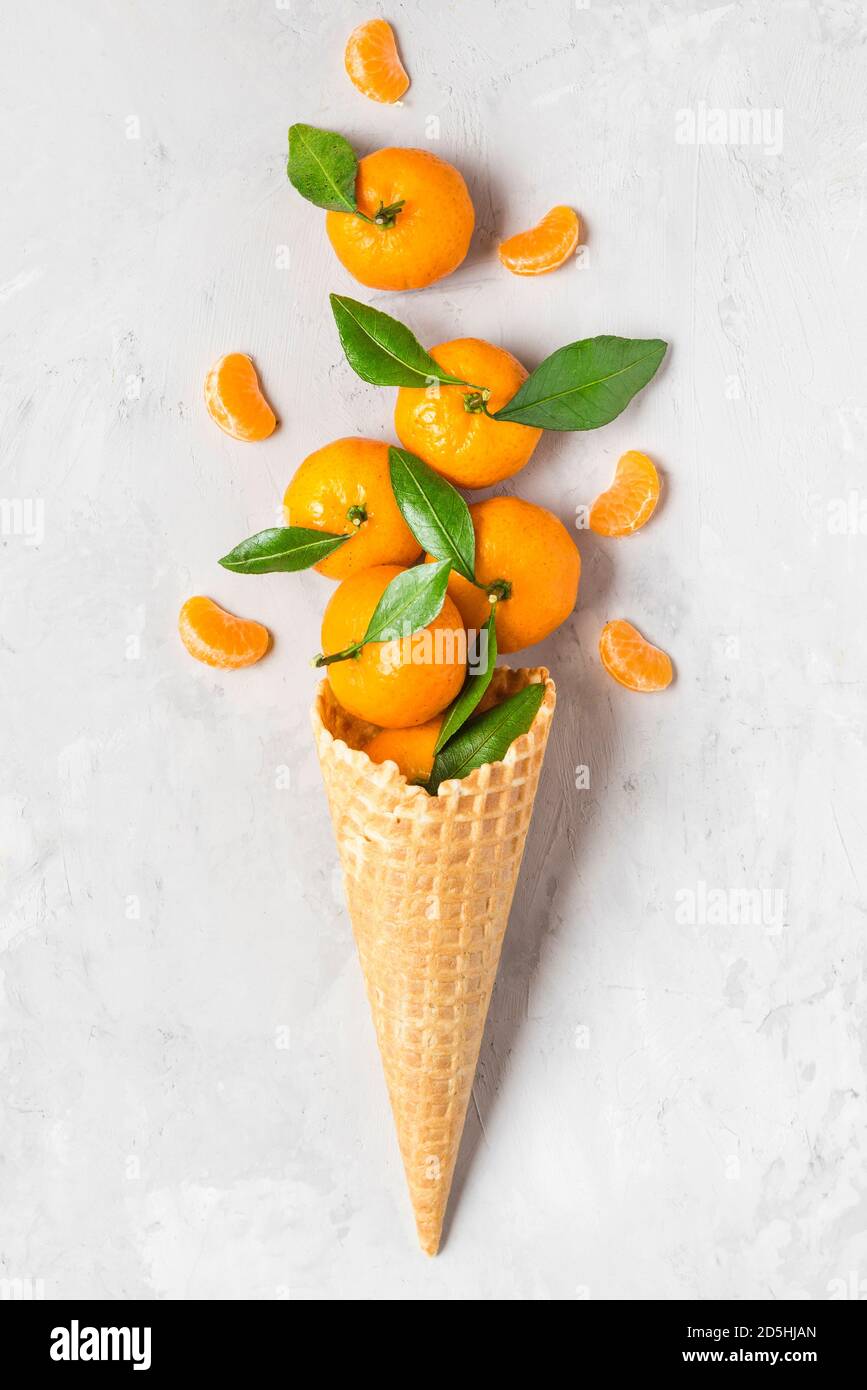 mandarin orange or tangerine fruits in waffle ice cream cone with slices on concrete background. winter Christmas food concept. top view. flat lay. ve Stock Photo