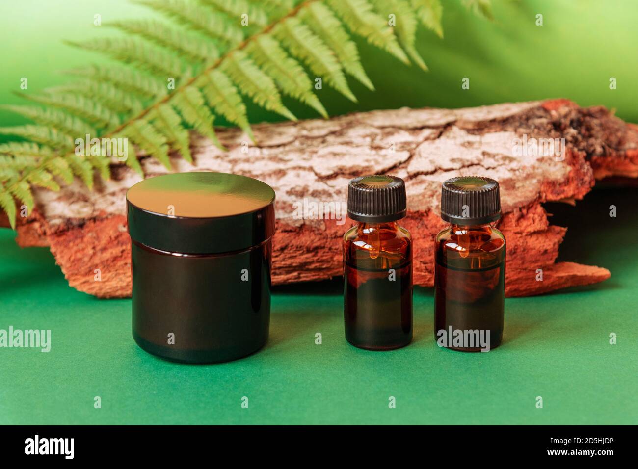 Cream jar and essential oils on green background with wood and greenery