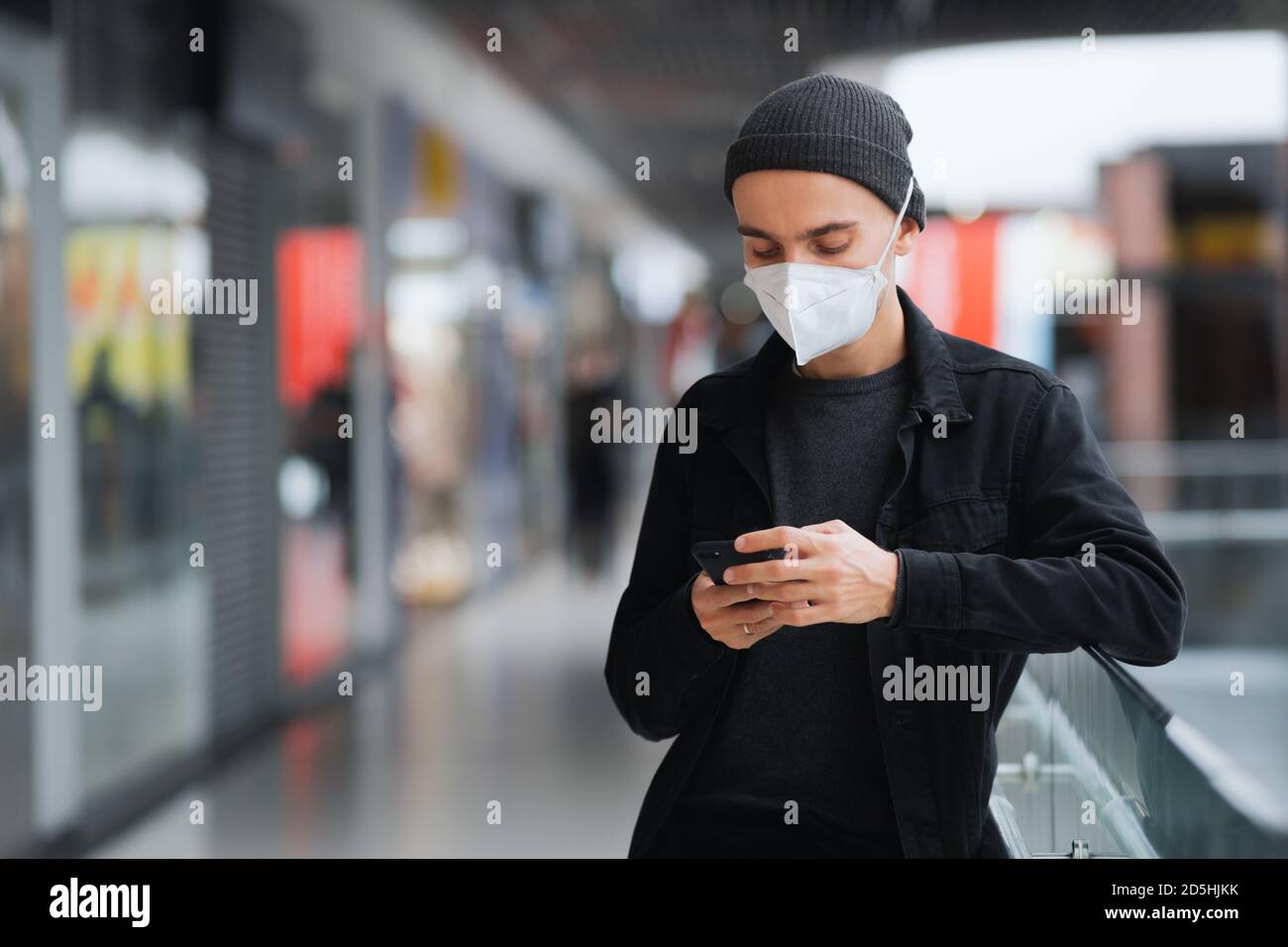 Man in protective mask with cell phone at a shopping centre or underground. Living in pandemic world, urban scene Stock Photo