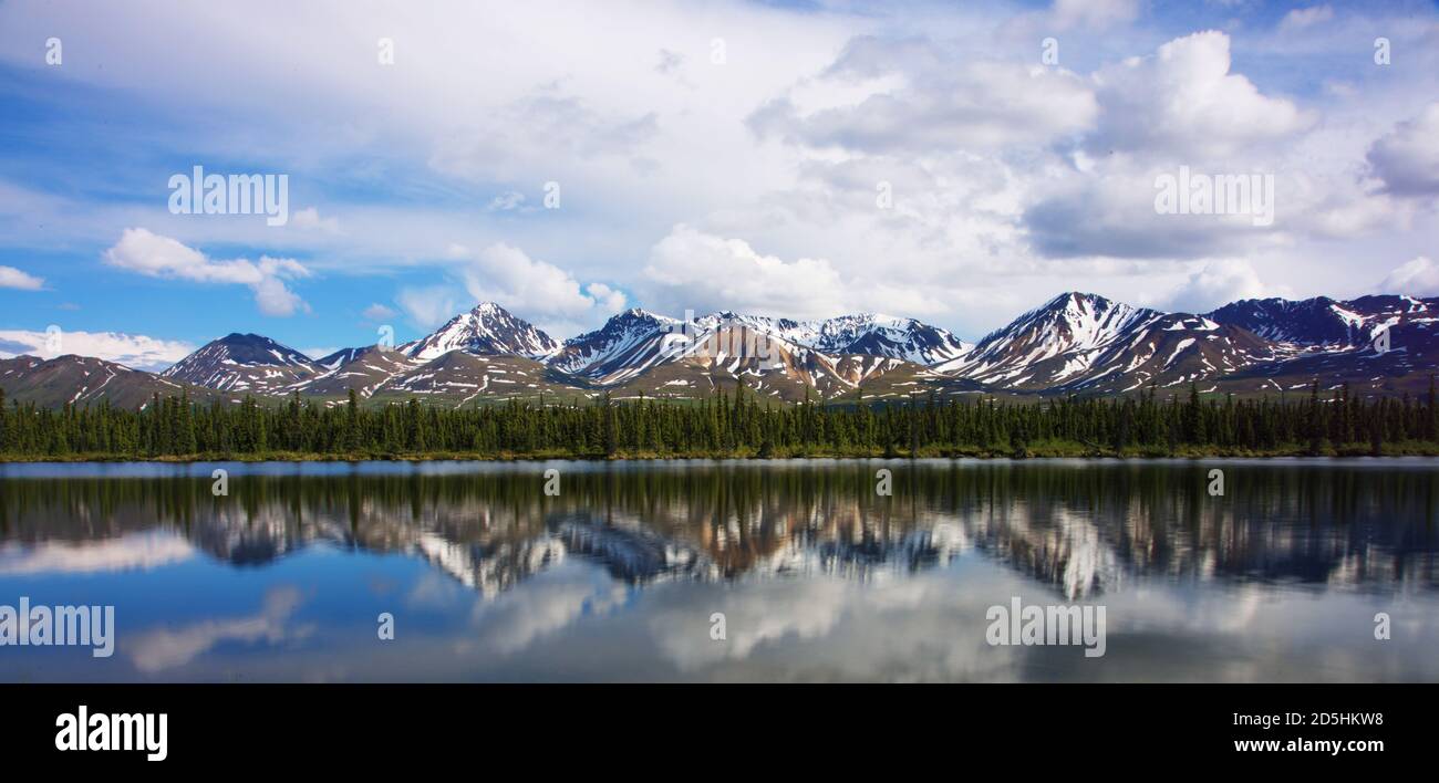 Jagged snowy mountain peaks with snow on the top reflected in shallow river  during early summer Stock Photo - Alamy, image size:1300x708