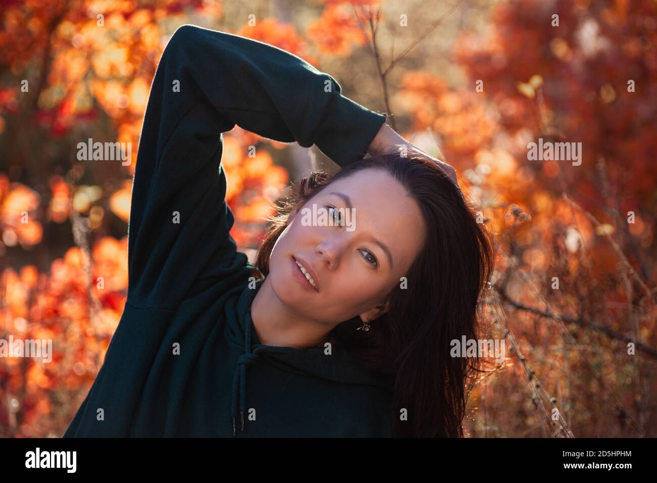portrait of smiling beautiful Asian young woman playing with her hair in the autumn forest at sunset Stock Photo
