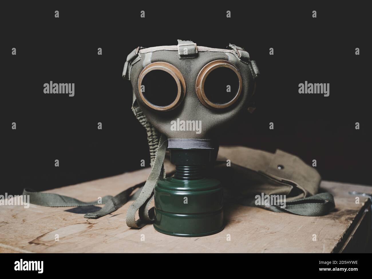 An old military gas mask on wood surface. Side view, flat. Dark background. Stock Photo
