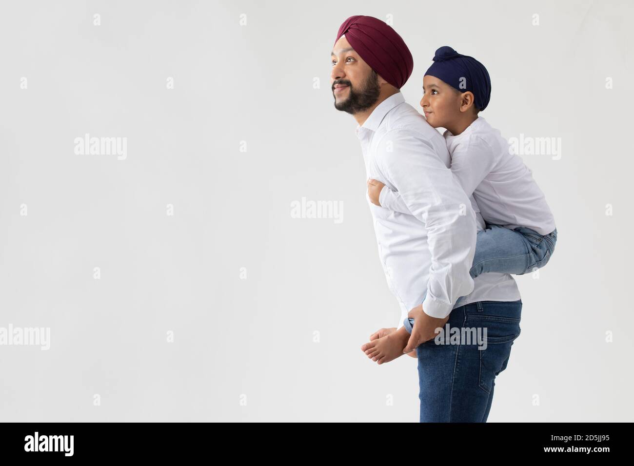 A SIKH FATHER CARRYING SON ON BACK AND LOOKING AHEAD Stock Photo