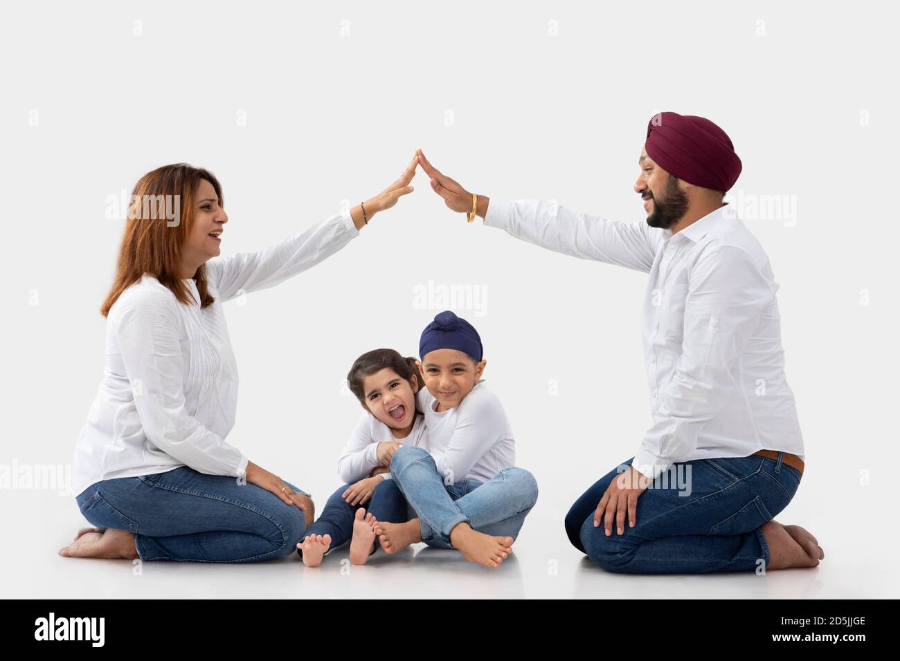 SIKH BROTHER AND SISTER HUGGING EACH OTHER LAUGHING WHILE MOTHER FATHER ARE SITTING AND HOLDING HANDS TO MAKE HOUSE Stock Photo