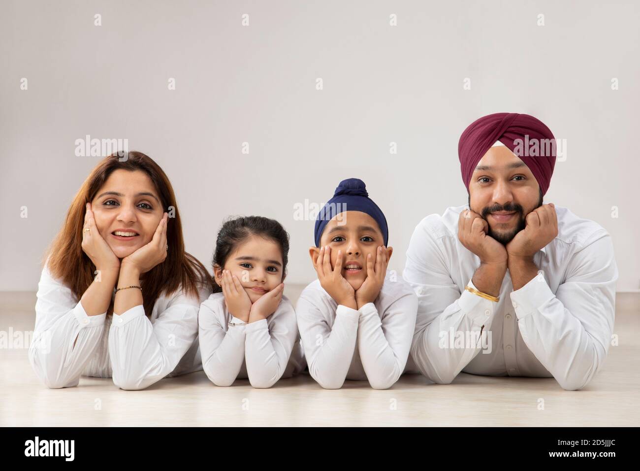 A SIKH FAMILY HAPPILY LOOKING AT CAMERA AND POSING BY LEANING ON GROUND AND HANDS RESTING ON CHIN Stock Photo