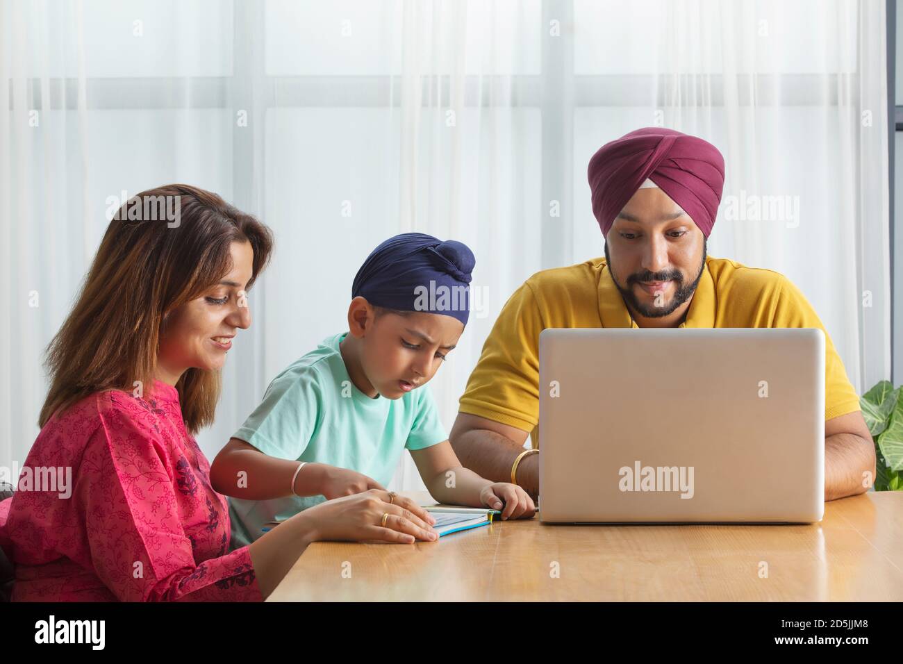 A SIKH BOY READING WITH MOTHER WHILE FATHER IS WORKING ON HIS LAPTOP Stock Photo