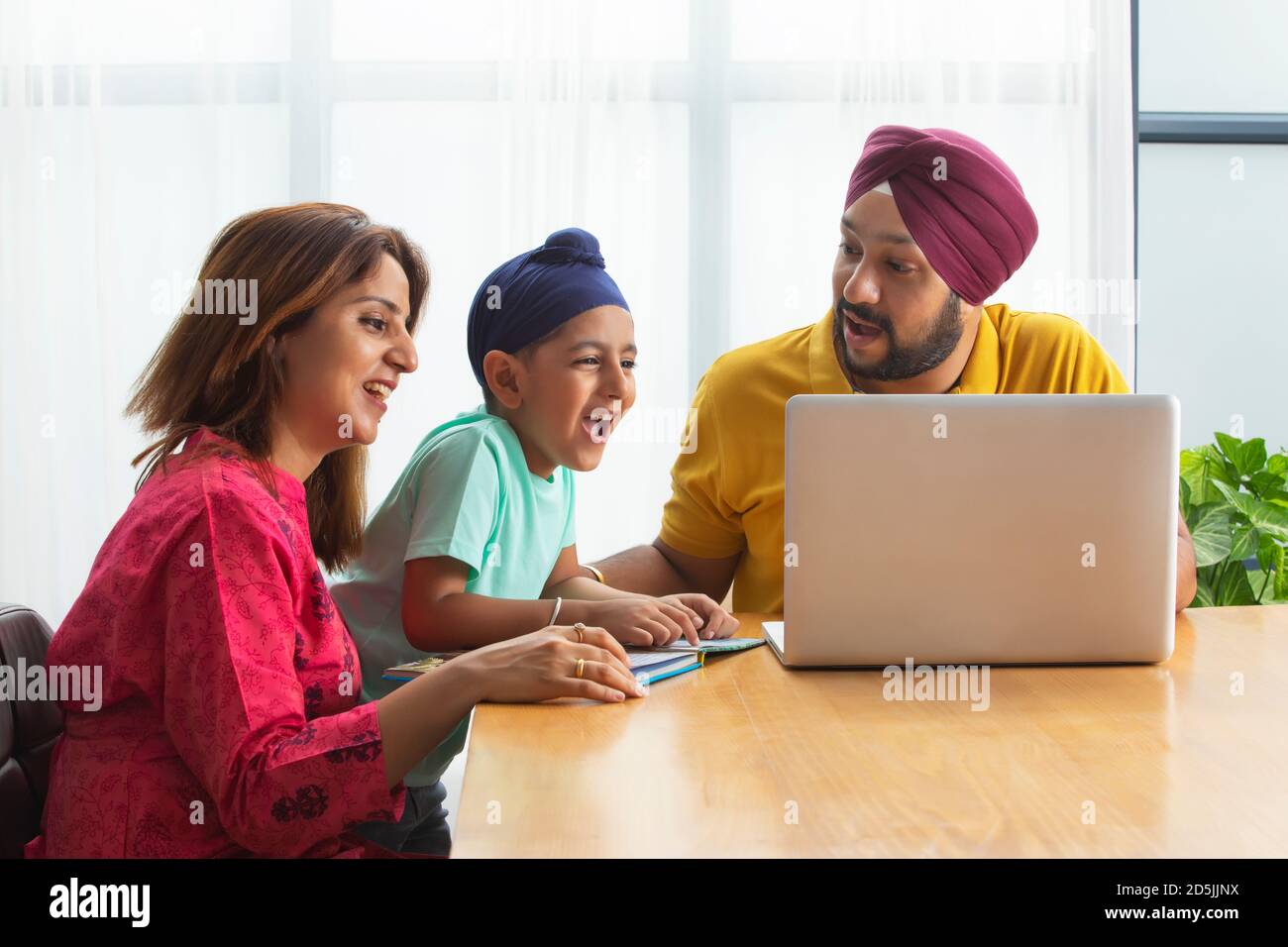 A SIKH BOY ENTHUSIASTICALLY LEARNING WHILE PARENTS TEACH HIM USING LAPTOP Stock Photo