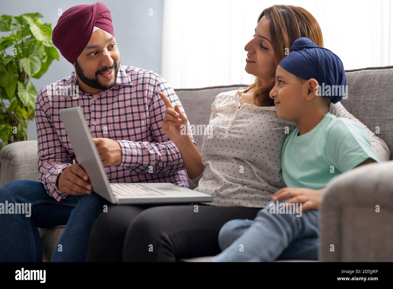 A SIKH PARENTS LOOKING AT EACH OTHER WHILE TEACHING SON WITH LAPTOP Stock Photo
