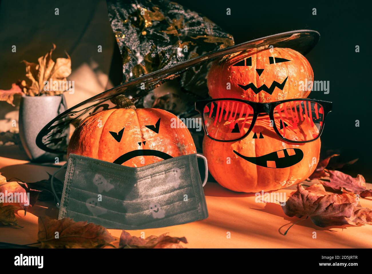 Three halloween pumpkins painted as Jack's lantern in festive bloody glasses, hat, face mask with leaves and shadows. Stock Photo