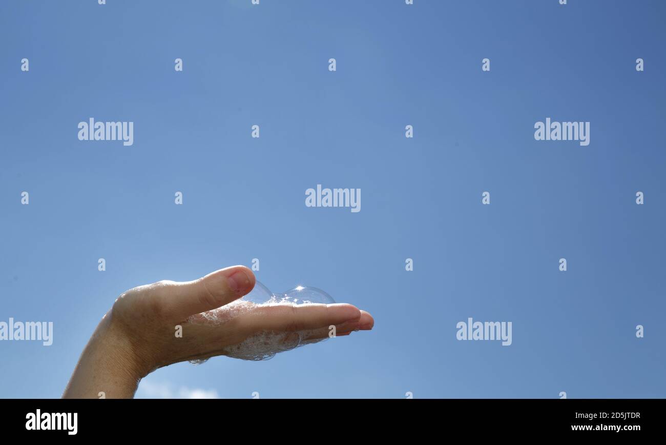 Closeup Female hand palm up with soap bubbles on blue sky background  Stock Photo
