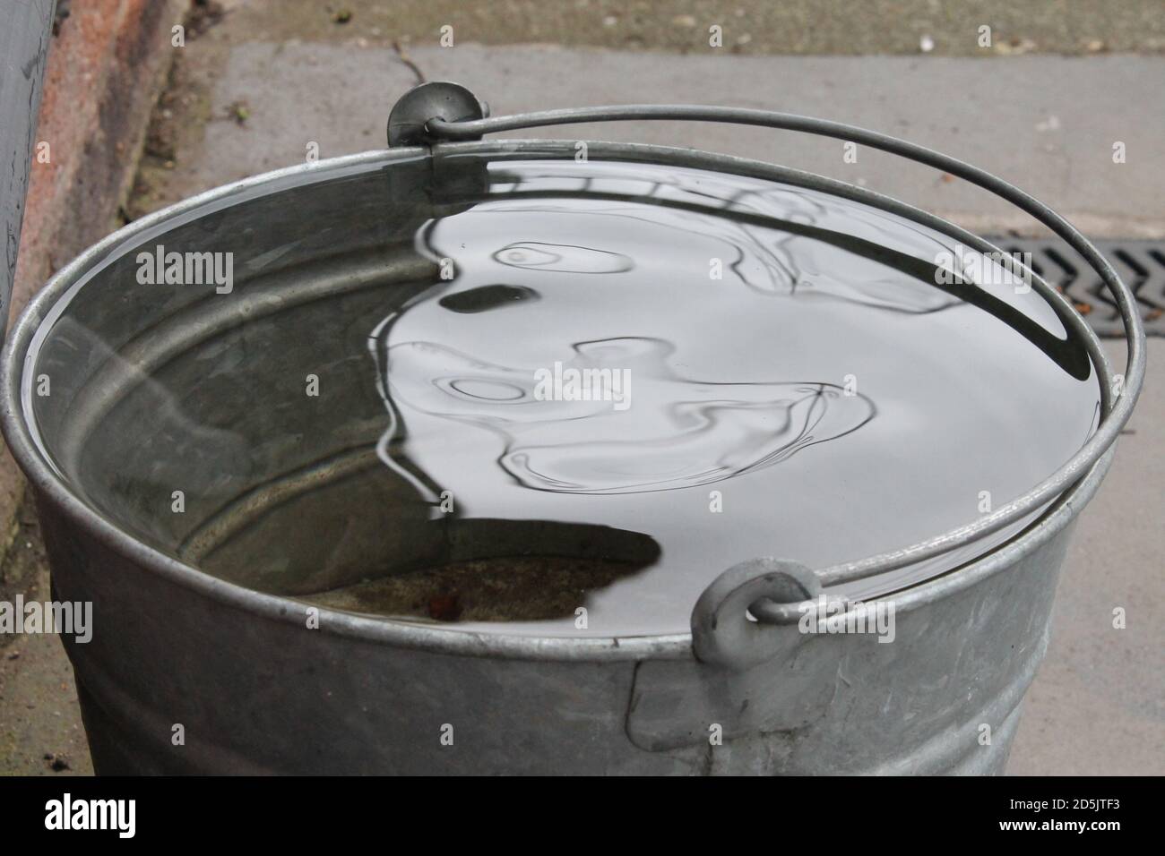 Galvanised metal bucket full of rain water with wind ripple and