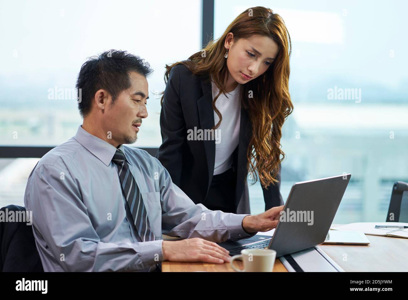 asian businessman and businesswoman having a discussion in office using laptop computer Stock Photo