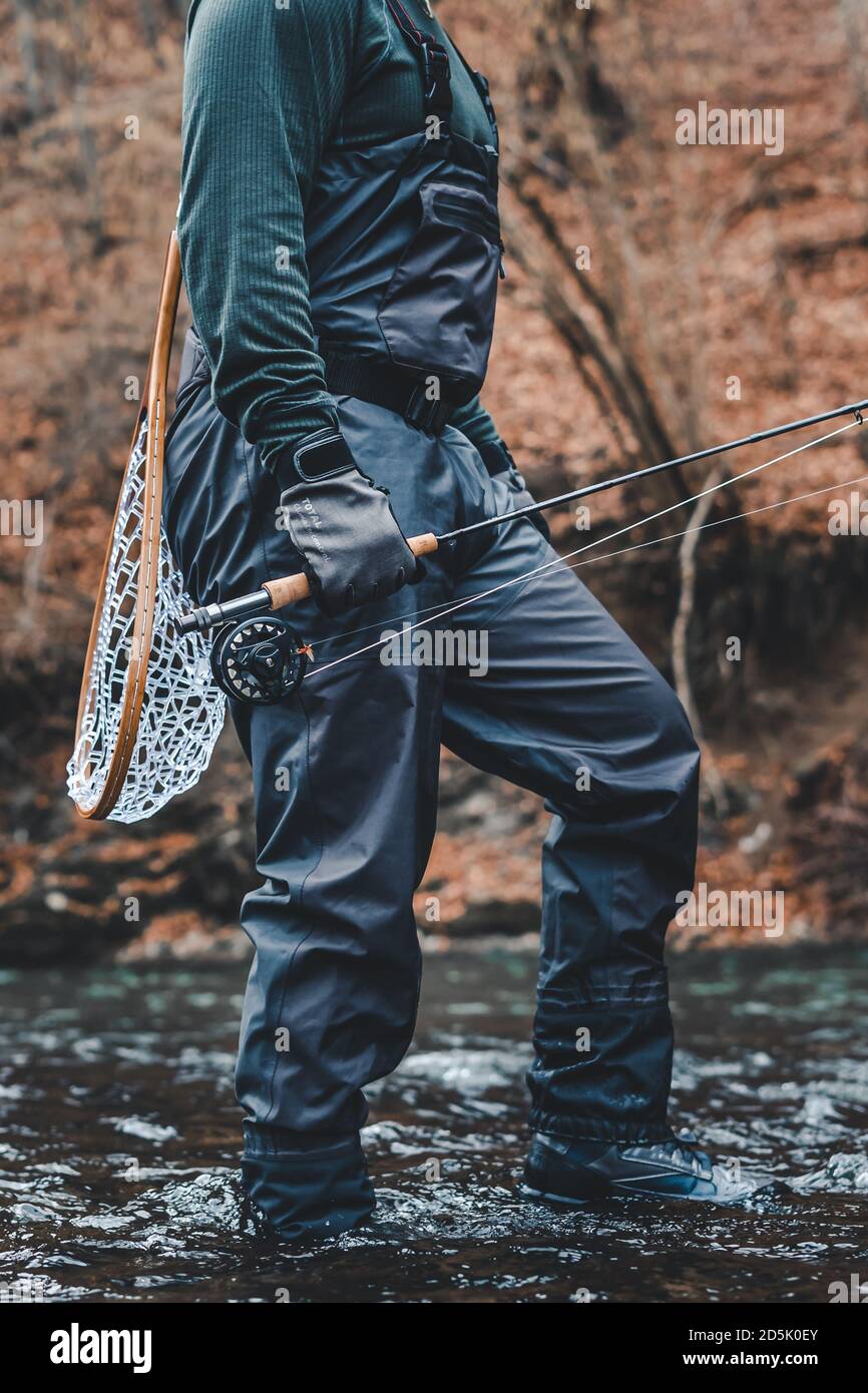 Fisherman fly fishing in river with rod, reel and landing net Stock Photo