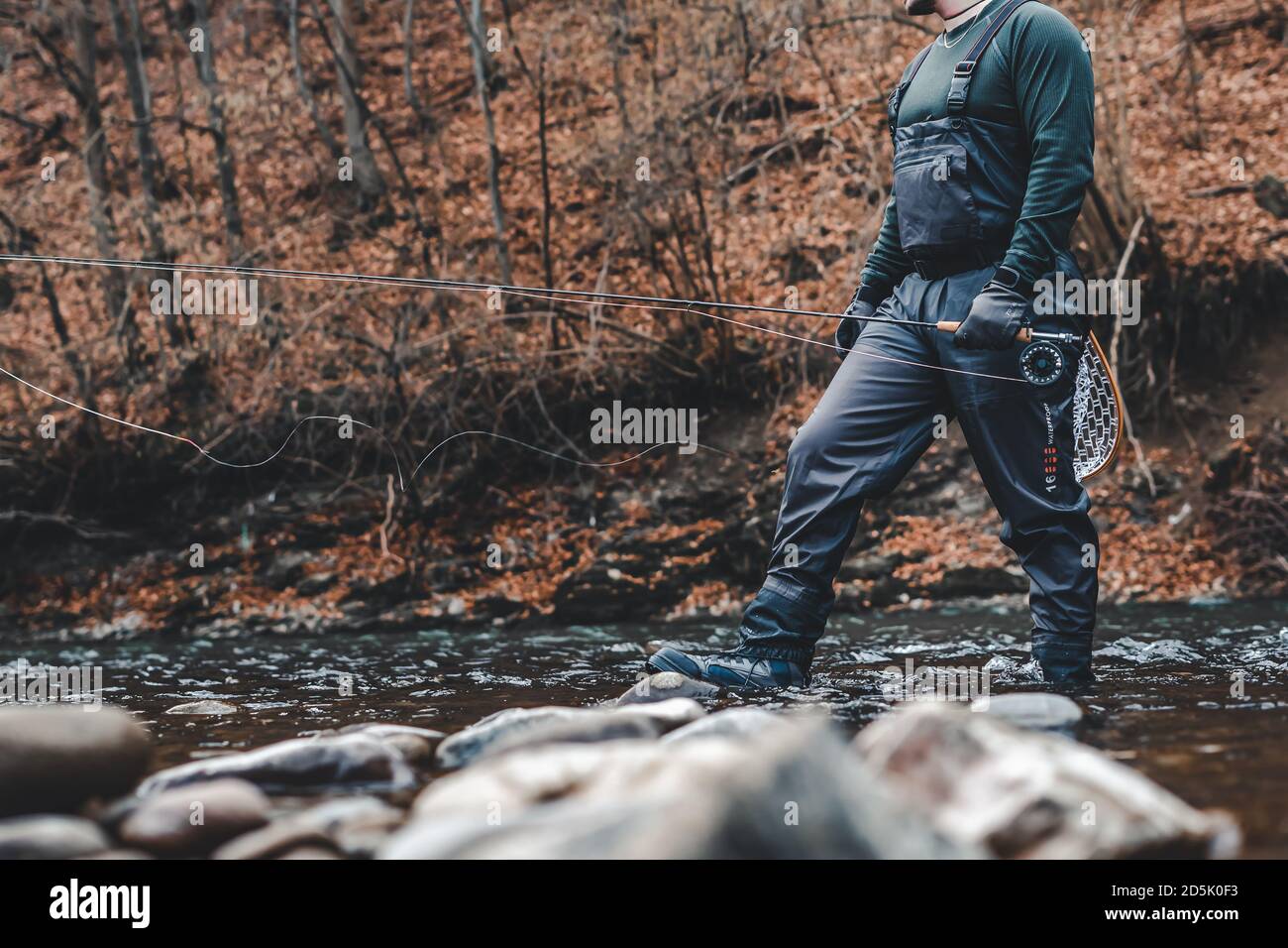 Fisherman fly fishing in river with rod, reel and landing net. Stock Photo
