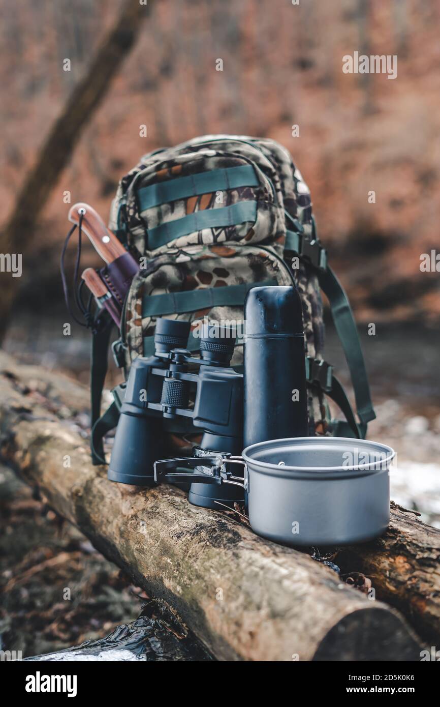 Backpack, knife, binocular, thermos and pot on wood. Hiking, travel or survival gear. Stock Photo