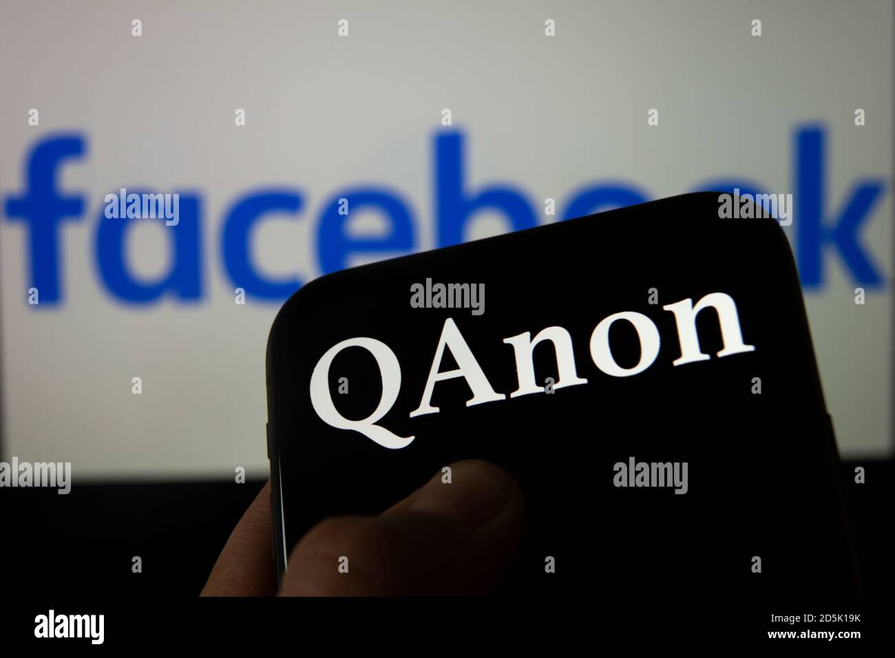 QAnon vs FACEBOOK. QAnon organisation logo seen on the smartphone which is placed on Facebook logos. Concept for ban of QAnon on social media. Stock Photo