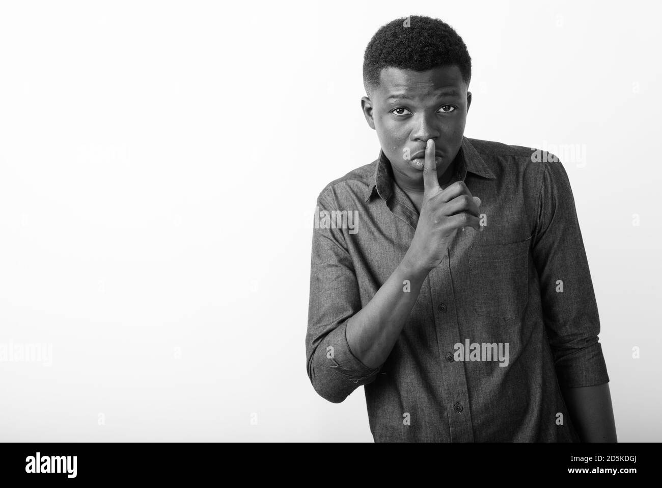 Studio shot of young black African man with finger on lips against white background Stock Photo
