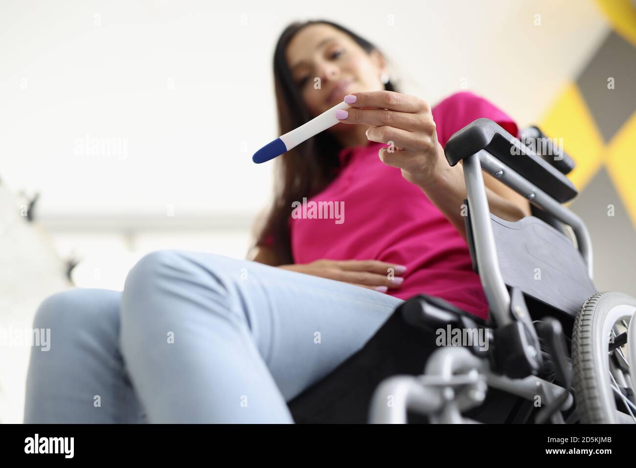 Woman in wheelchair is sitting and looking at pregnancy test Stock Photo