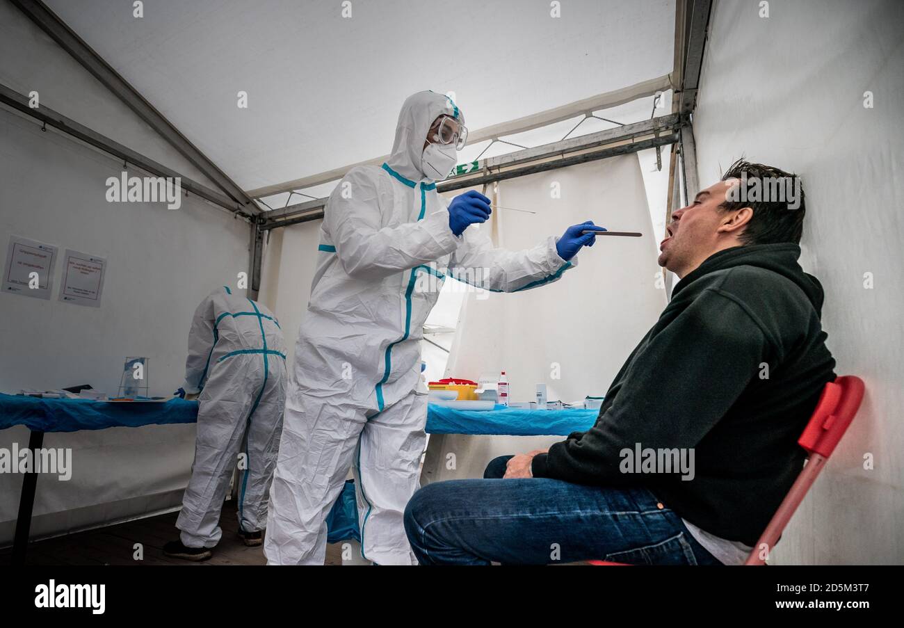 Berlin, Germany. 14th Oct, 2020. A member of the medical staff is doing a Covid-19 smear on a man. At the Corona Test Centre at the Ärztehaus Mitte, citizens without corona symptoms can be tested in a tent in the car park in front of the doctor's practice, for example, to be able to present a test result that is as negative as possible for travel or for professional reasons. Credit: Michael Kappeler/dpa/Alamy Live News Stock Photo