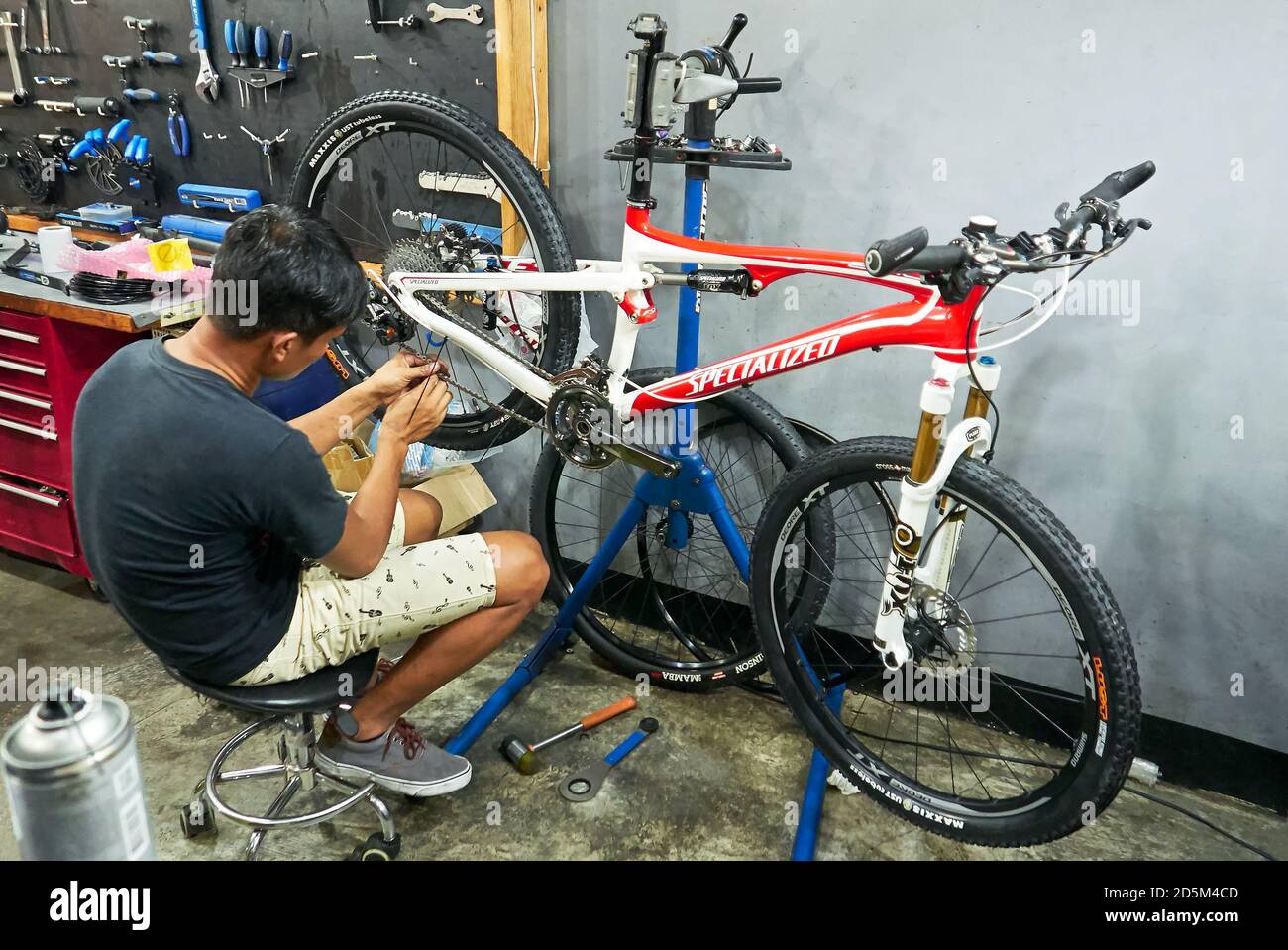 One young bike mechanic is repairing a Specialized Epic full suspension bike with professional tools in a clean workshop in the Philippines, Asia Stock Photo