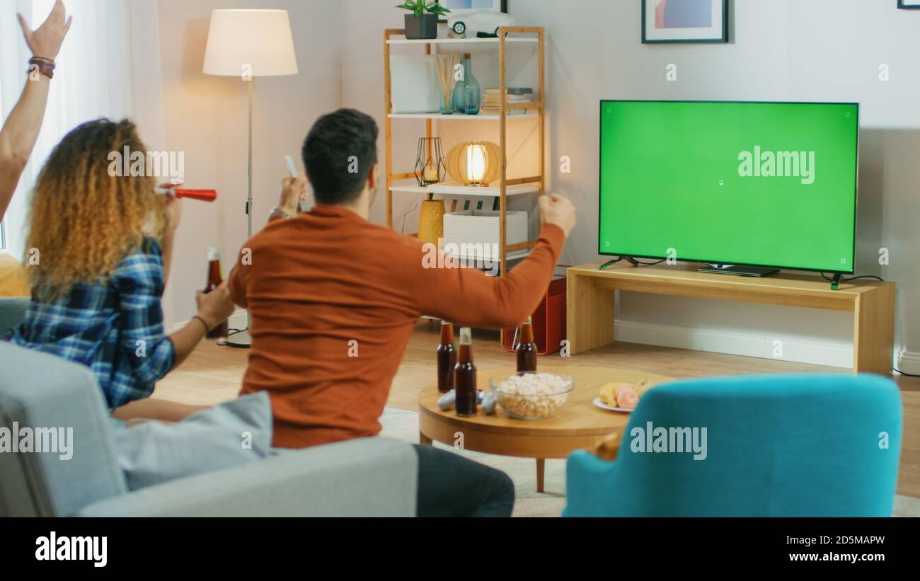 Three Sports Fans Sitting on a Couch in the Living Room Watch Green