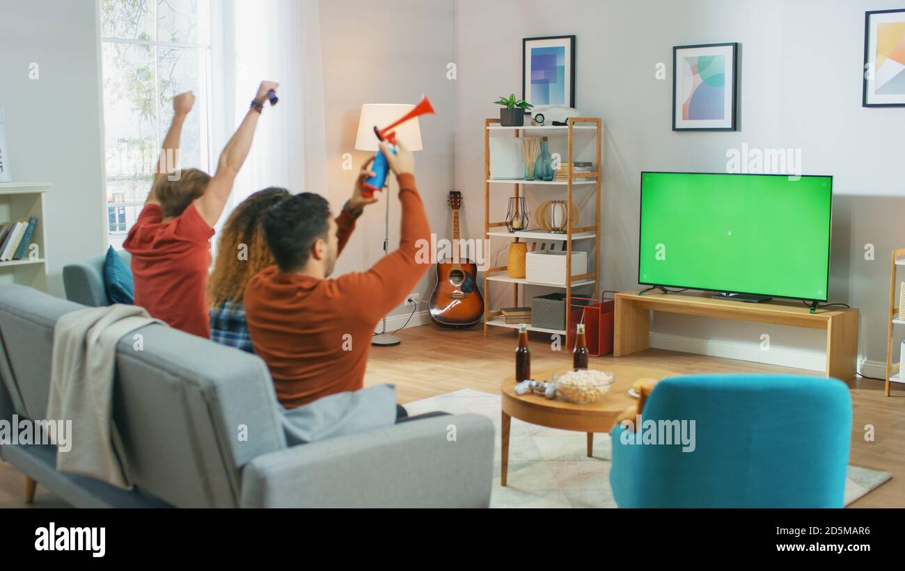 Three Sports Fans Sitting on a Couch in the Living Room Watch Green
