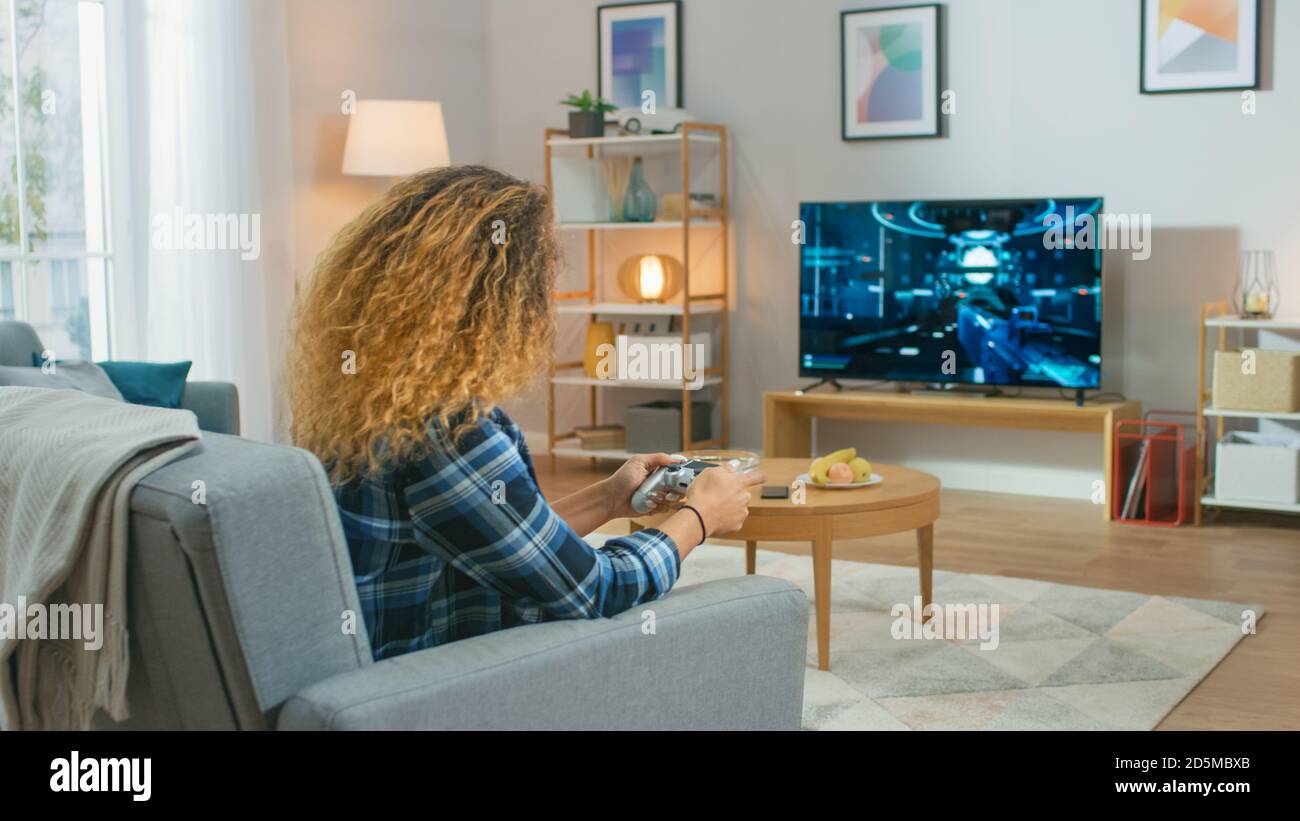 In the Living Room Girl Sitting on a Couch Holds Controller Playing in