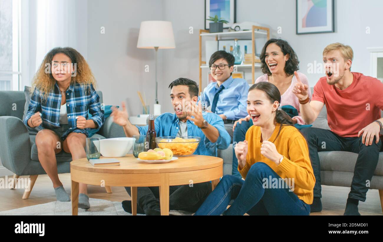 At Home Diverse Group of Sports Fans Sitting on a Couch Watching Important Sports Game Match on TV, They Cheer for the Team at a Very Tense Moment Stock Photo