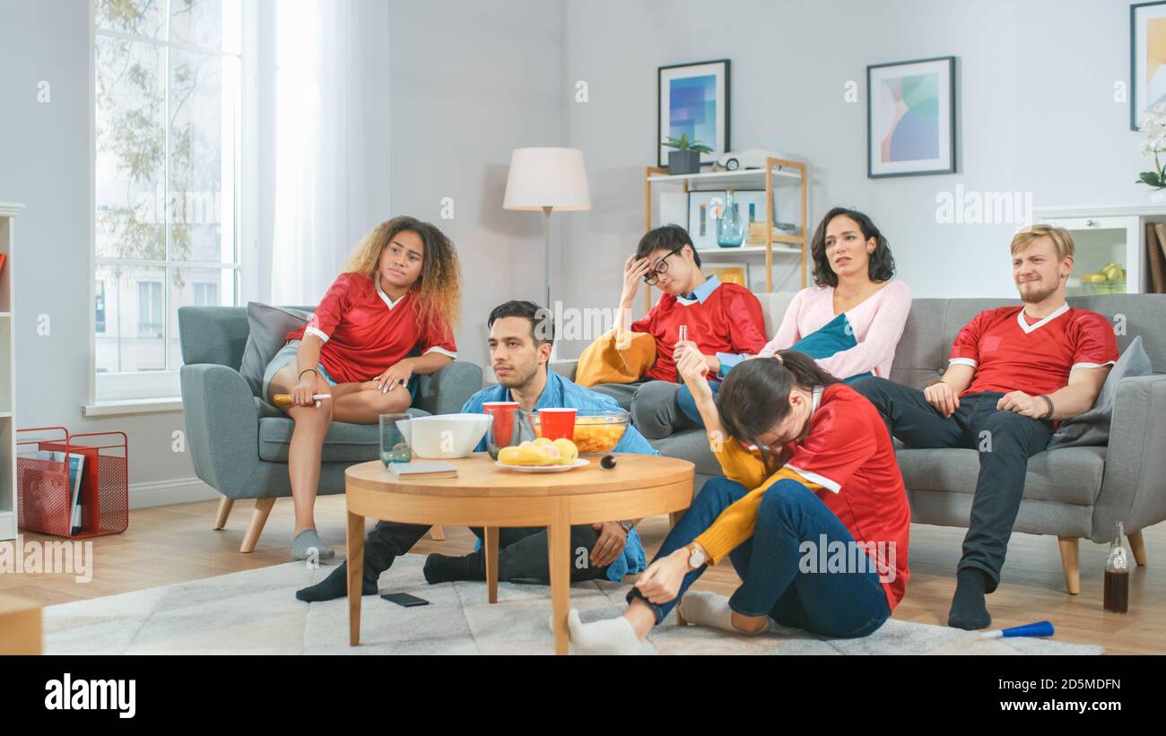At Home Diverse Group of Sports Fans Wearing Team's Uniform Watch Sports Game Match on TV, They Cheer but the Team Loses. Cozy Room with Snacks and Stock Photo