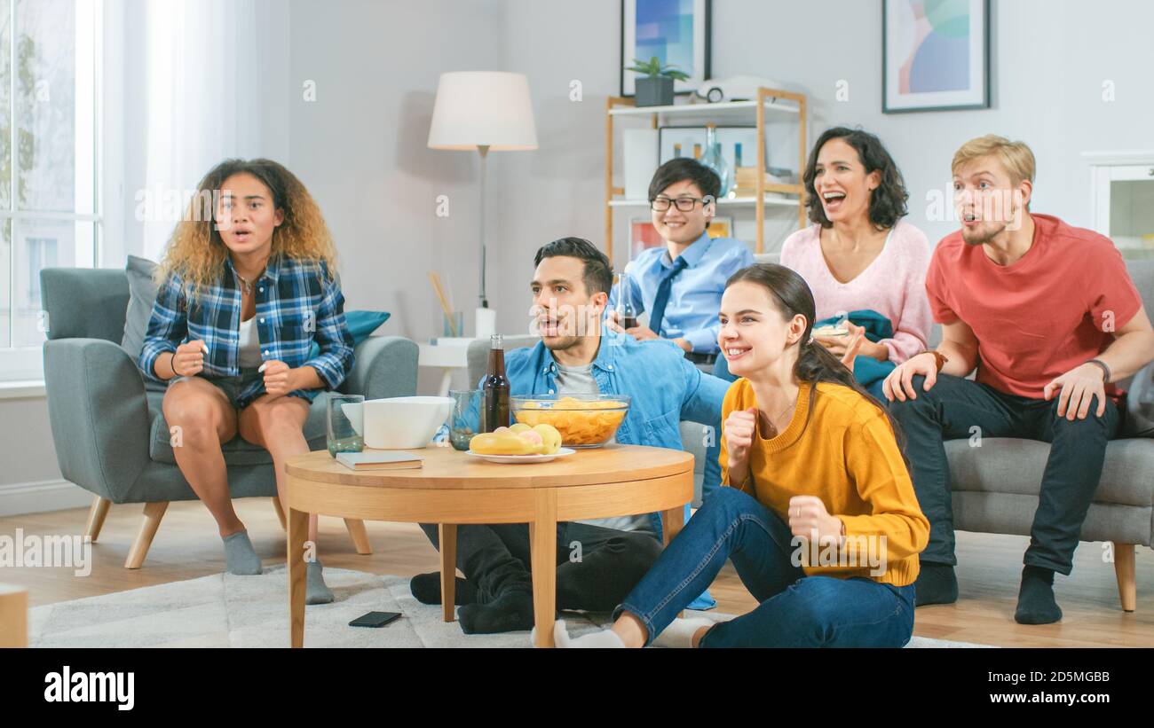 In the Living Room Diverse Group of Friends on Watching Sports Game Match on TV, They Cheer and Chant for the Team, Celebrate Victory after Team Stock Photo