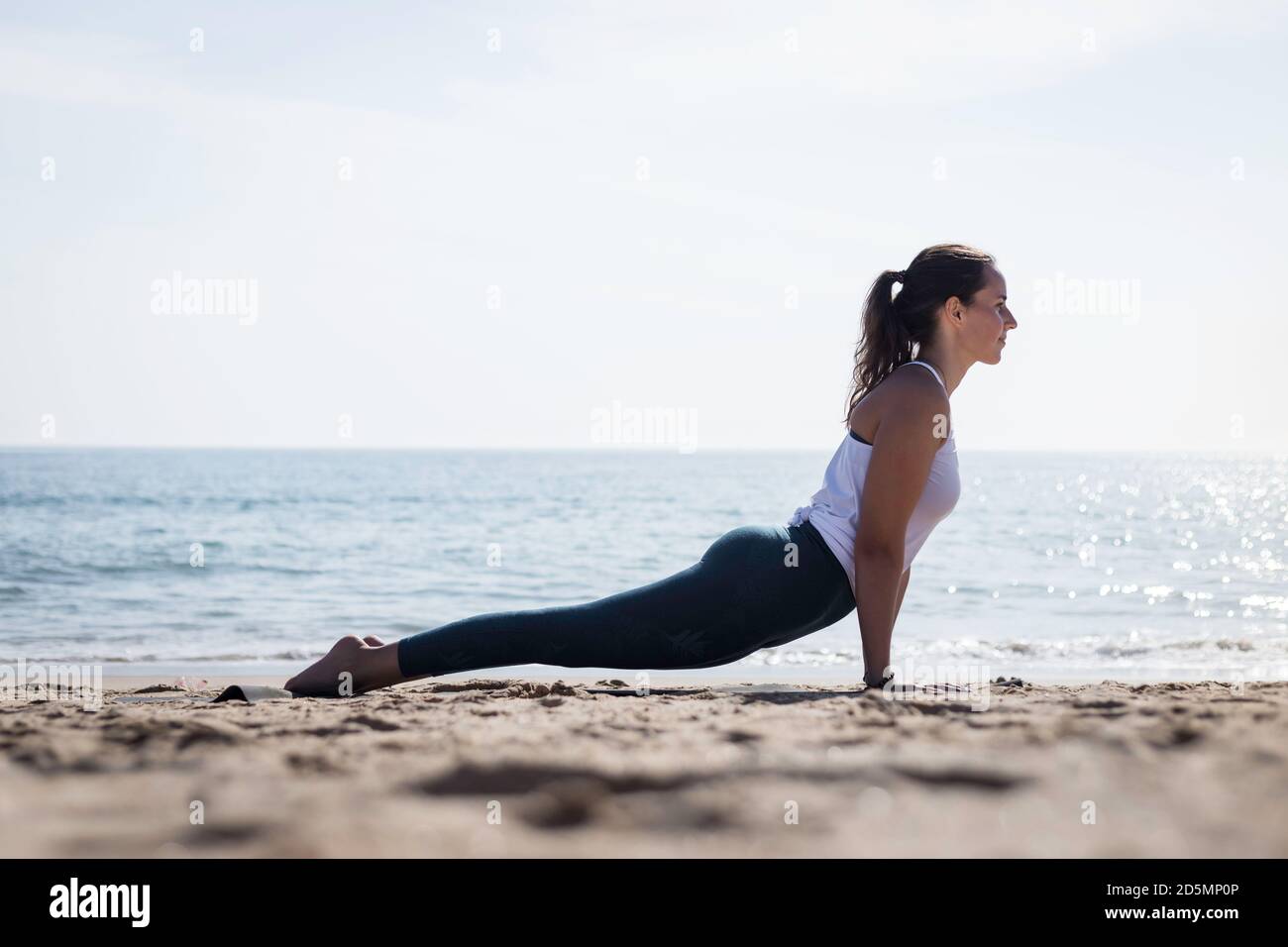 Sporty young woman doing Yoga exercises using a gym mat along the beach