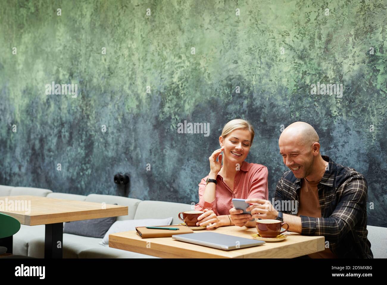 Young man using mobile phone while drinking coffee in cafe together with his girlfriend Stock Photo