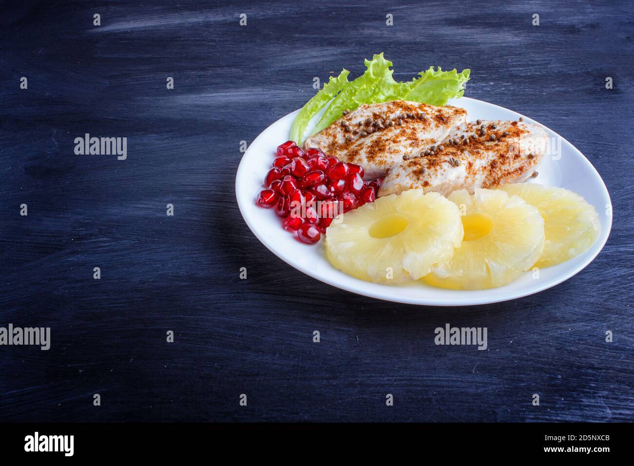 Fried chicken fillets with lettuce, pineapple and pomegranate seeds on black wooden background, copy space, top view. Stock Photo