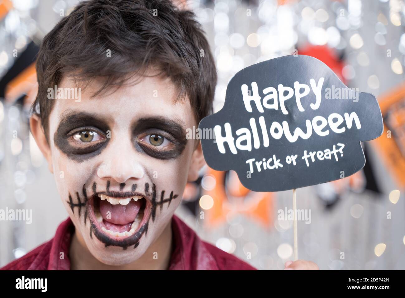 Kid hloding Halloween booth prop and making gesticulating spooky face - concept of halloween trick or treat. Stock Photo