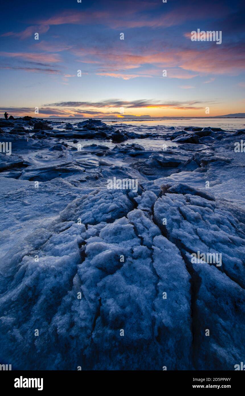 Sunset over the ocean from Coast in Iceland, with pink clouds and cracks in the Ice, Stock Photo