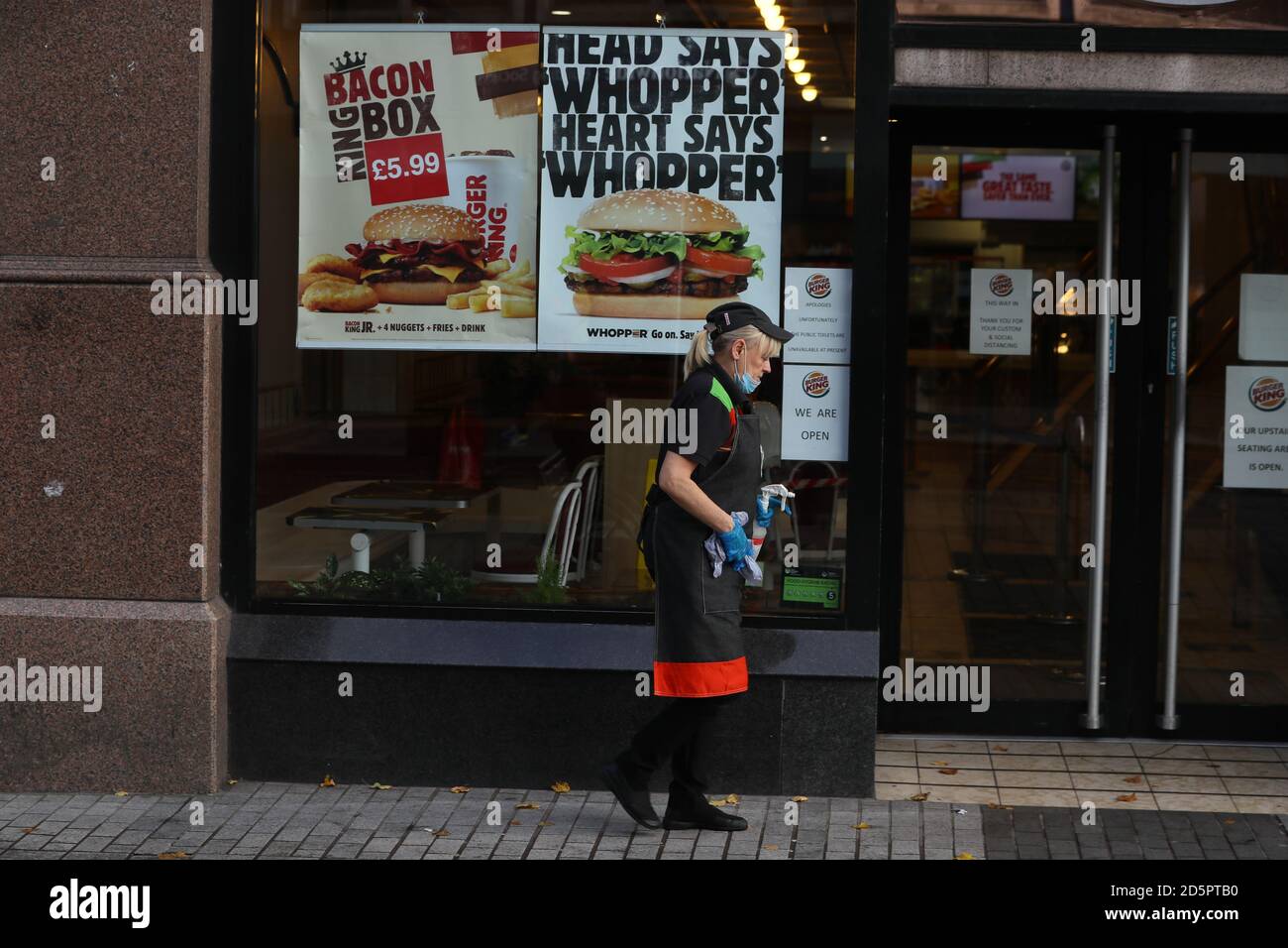 A Burger King employee cleans the outside of a branch in Belfast city centre, Northern Ireland, after the Stormont executive announced closures of schools, pubs and restaurants as the region enters a period of intensified coronavirus restrictions in response to spiralling infection rates. Stock Photo