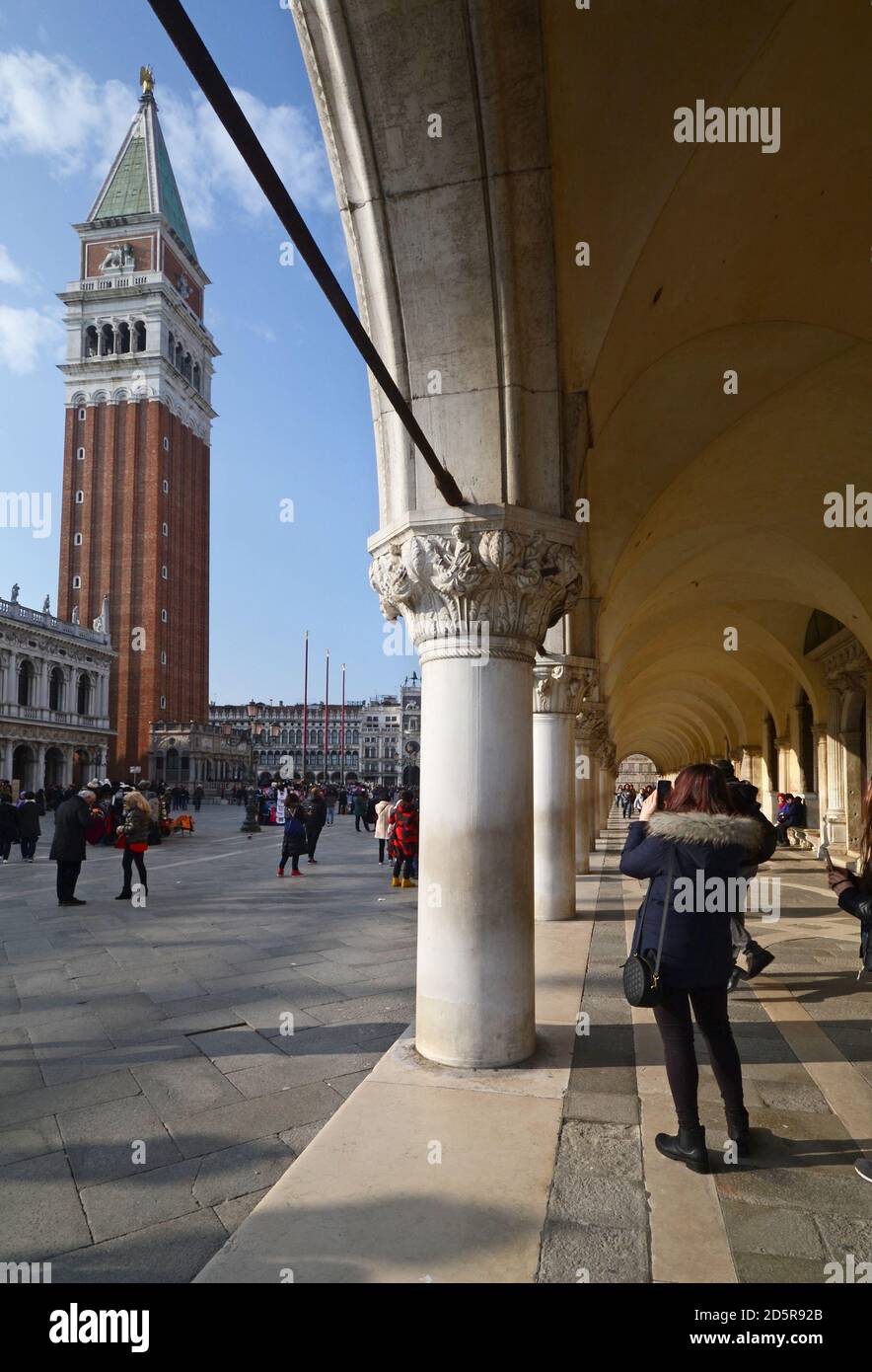 girl takes a picture with her smartphone at the bell tower in piazza san marco under a portico Stock Photo