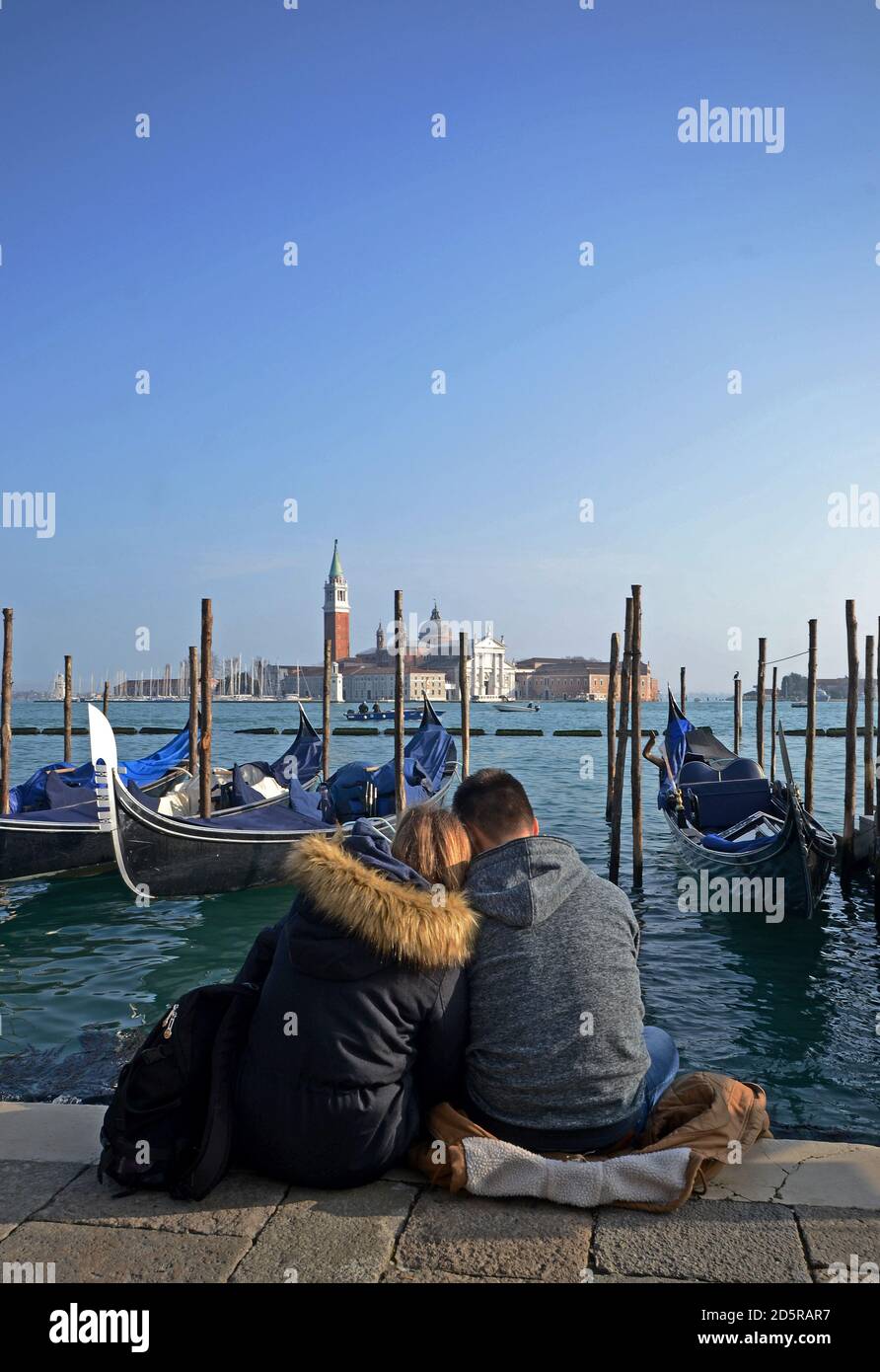 engaged young couple sitting along the bank of a canal. The church of San Giorgio in the background Stock Photo