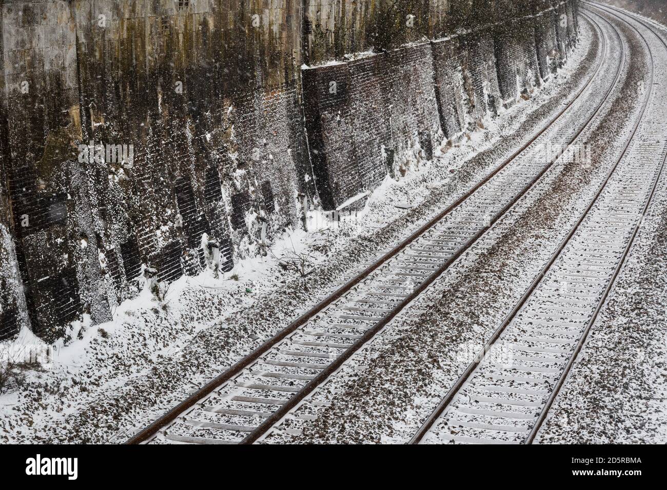 Railway tracks in winter alongside Victorian brick and stone wall Stock Photo