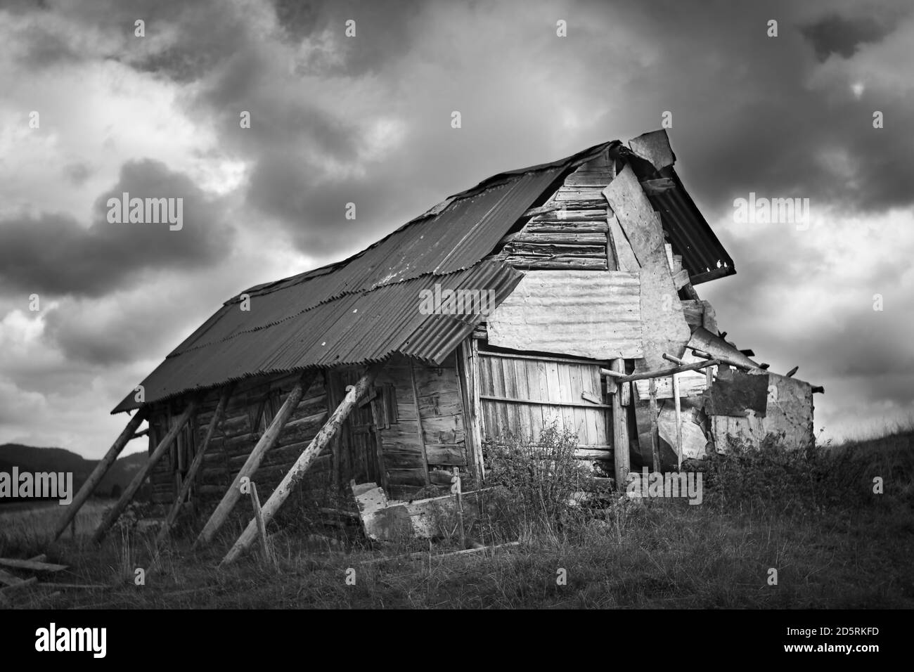 Black and white of old and dilapidated wooden and metal shack in the mountains of the Asiago plateau. Stormy sky. Enego, Vicenza, Italy Stock Photo