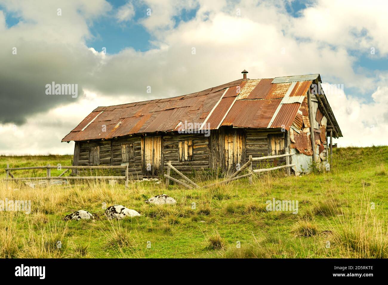 Old and dilapidated wooden and metal shack in the mountains of the Asiago plateau. Green meadow and stormy sky. Enego, Vicenza, Italy Stock Photo