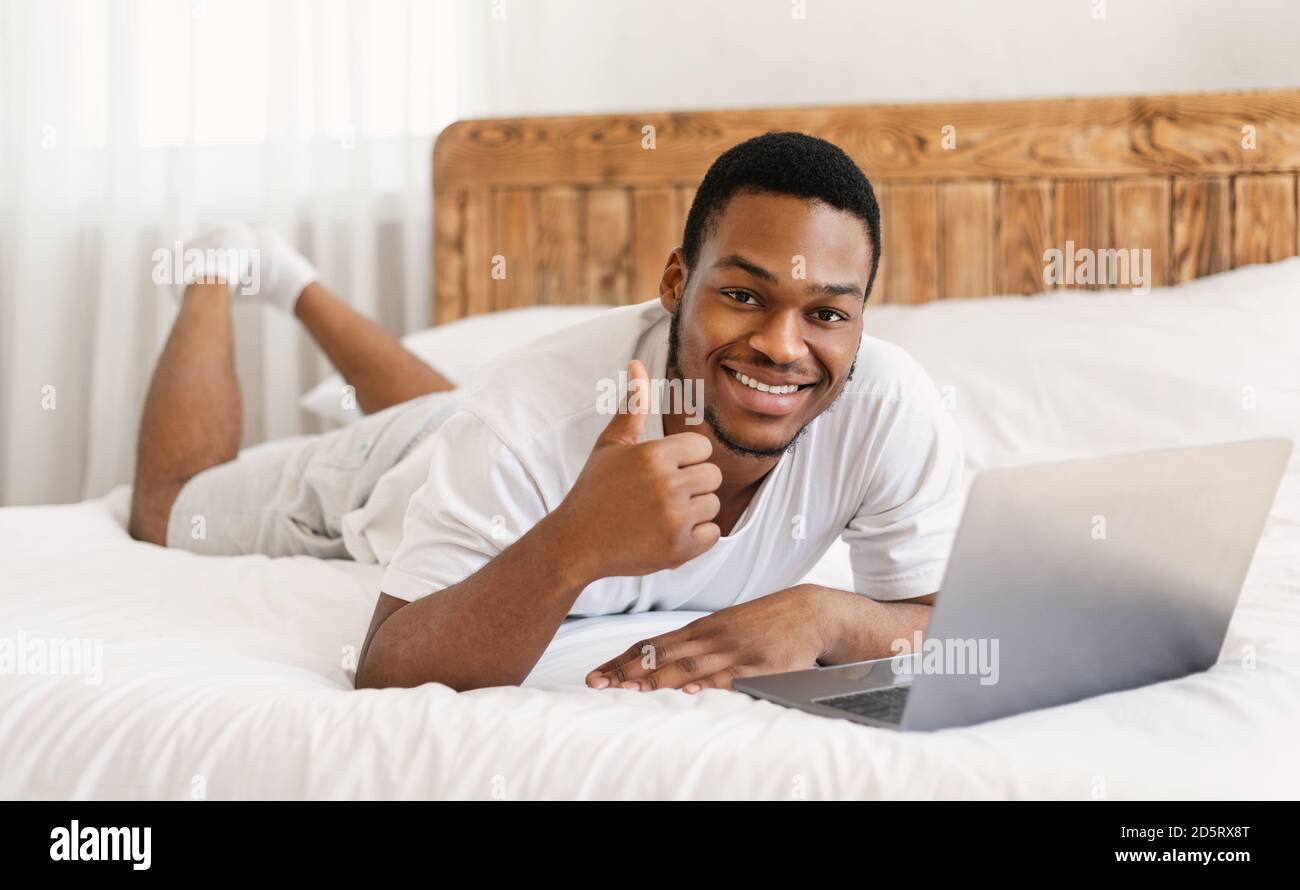 Black Man With Laptop Gesturing Thumbs-Up Working Lying In Bed Stock ...