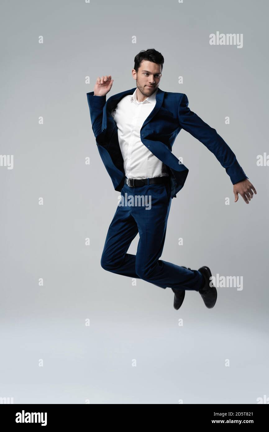 Fulllength photo of funny man in suit running or jumping in air isolated over gray background