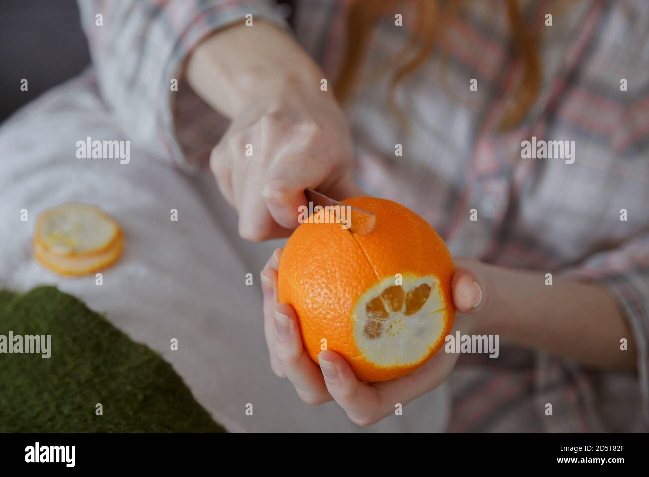 Close up view on women hand peeling an orange by segments with knife Stock Photo