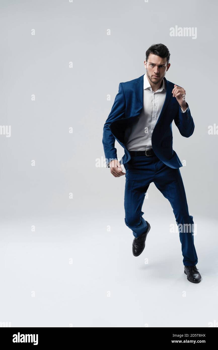 Fulllength photo of funny man in suit running or jumping in air isolated over gray background