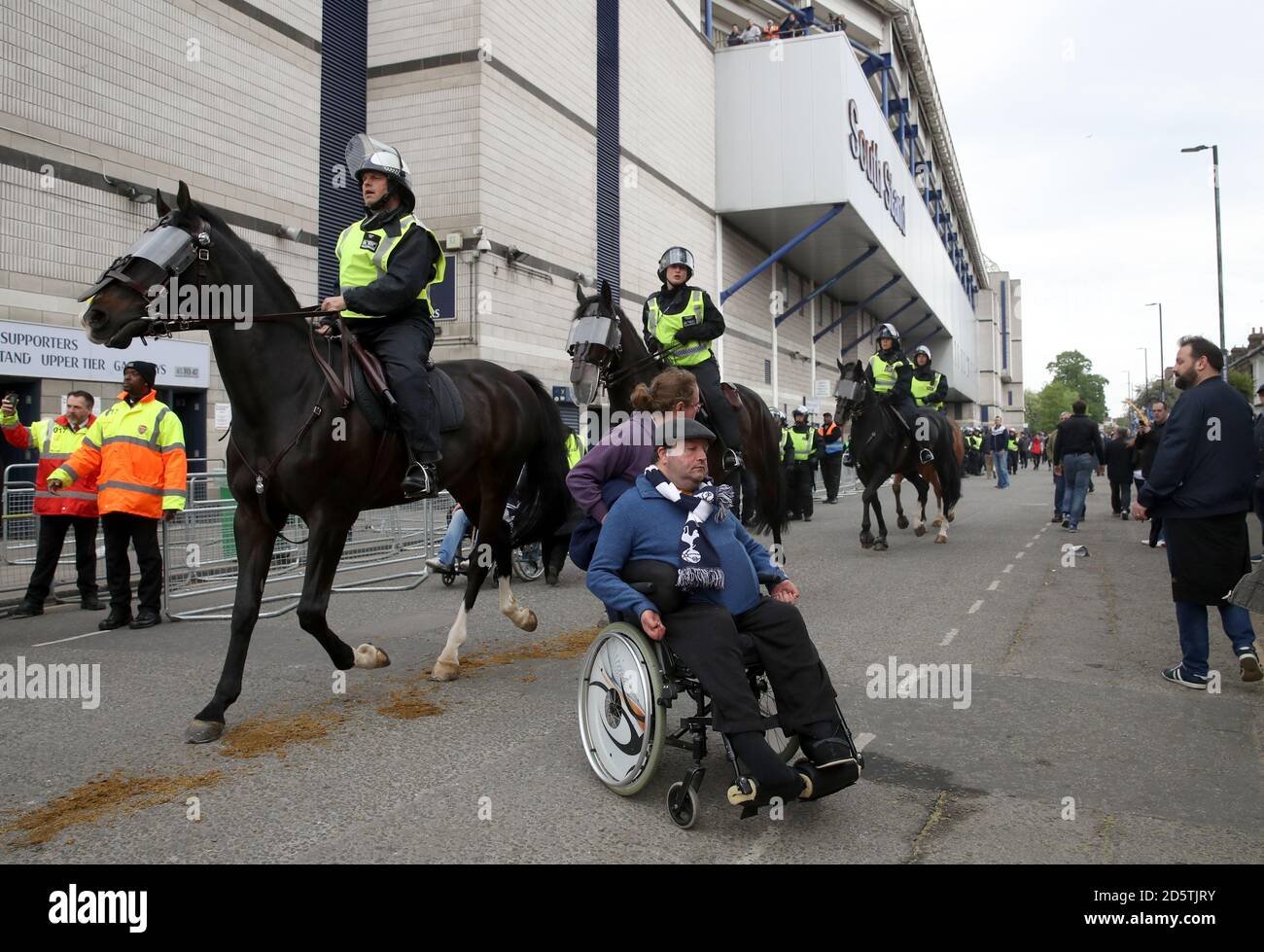 A disable Tottenham Hotspur fan in a wheelchair moves away from rushing mounted horsebacked police outside White Hart Lane Stock Photo