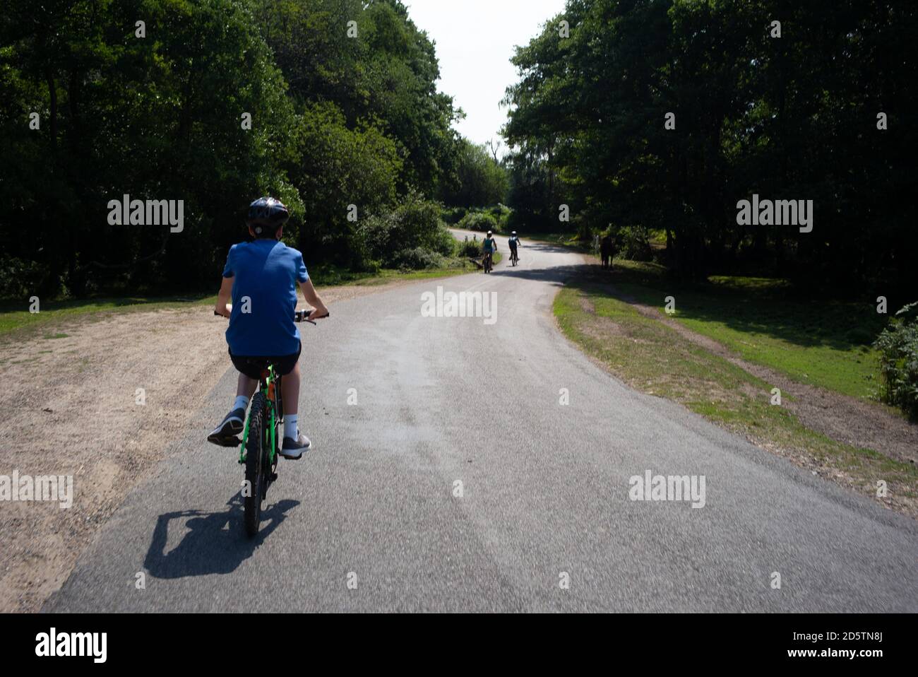 A teenage boy follows his family but lags behind down a country road in the New Forest Hampshire England on a family bike ride Stock Photo